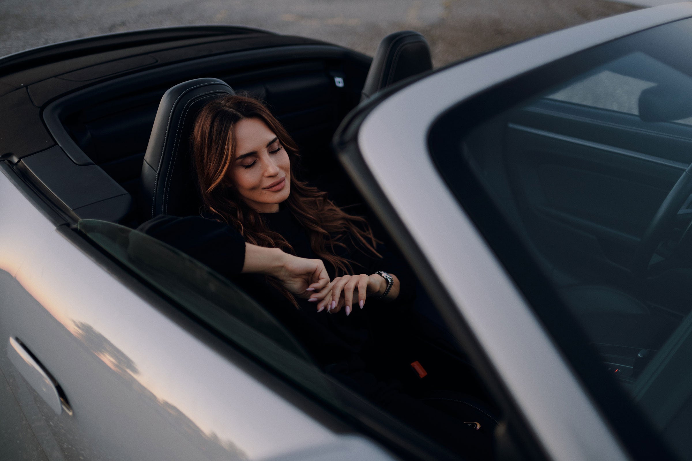 Woman sitting in a car with the top down, enjoying the open air.