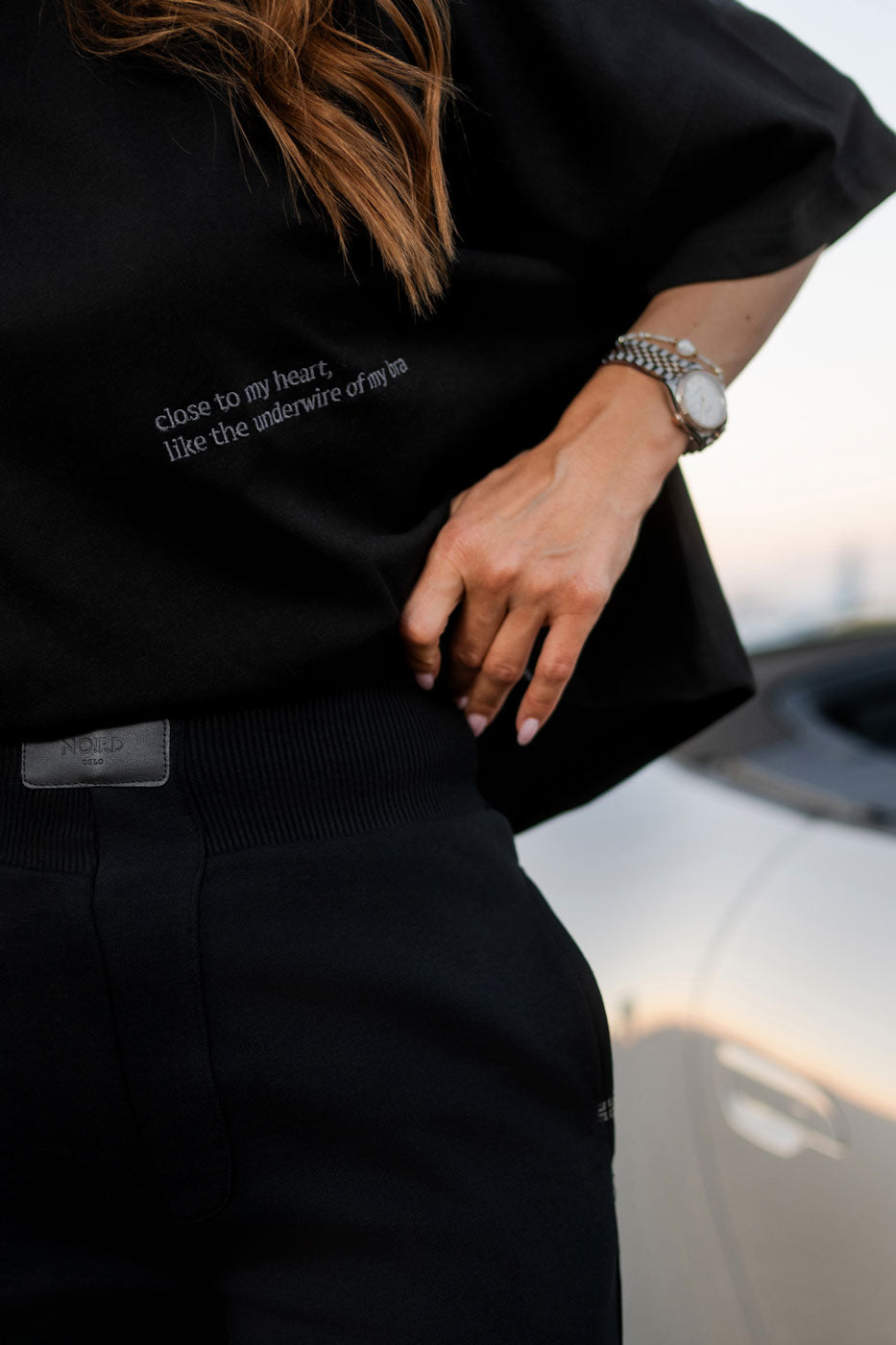 Embroidered line "close to my heart like the underwire of my bra" on women's NOIRD black cotton t-shirt