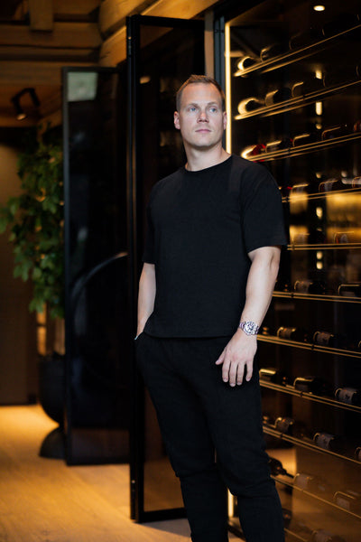 Man wearing NOIRD men's black cotton t-shirt, front view in wine cellar
