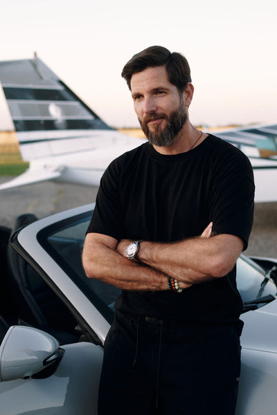 Man in NOIRD men's black cotton t-shirt next to car at dusk, relaxed fit